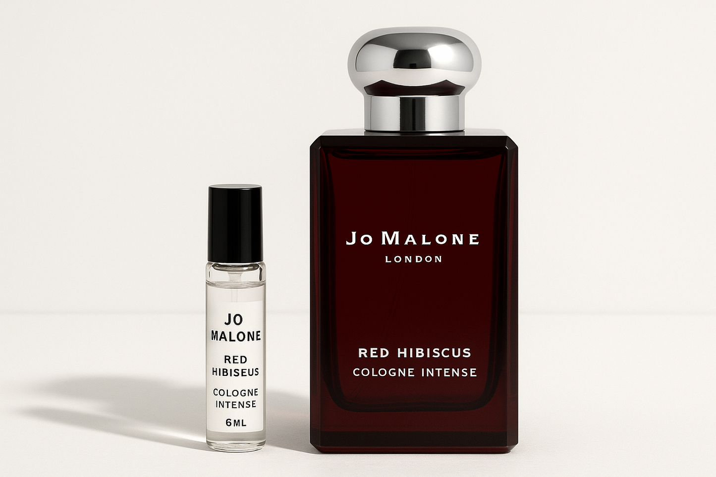 Jo Malone Red Hibiscus Cologne Intense 6ml sample standing next to 100ml perfume bottle of Jo Malone Red Hibiscus Cologne Intense which has white writing on dark red bottle